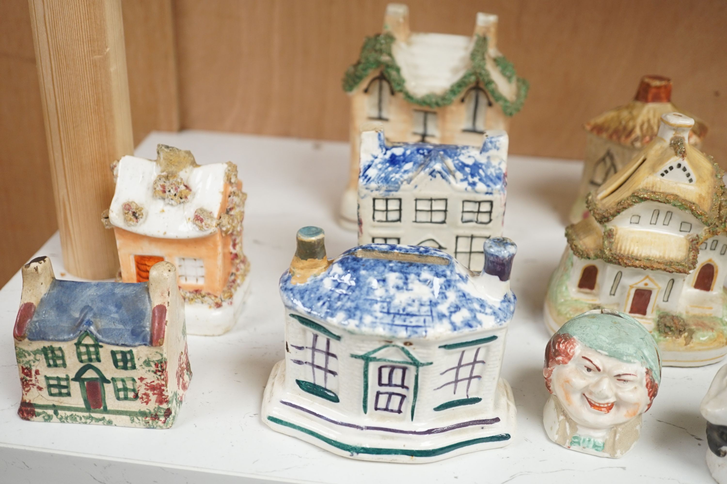 Twelve Staffordshire pottery money boxes, three with sponged decoration, modelled as cottages or heads, tallest 13.5 cms high.